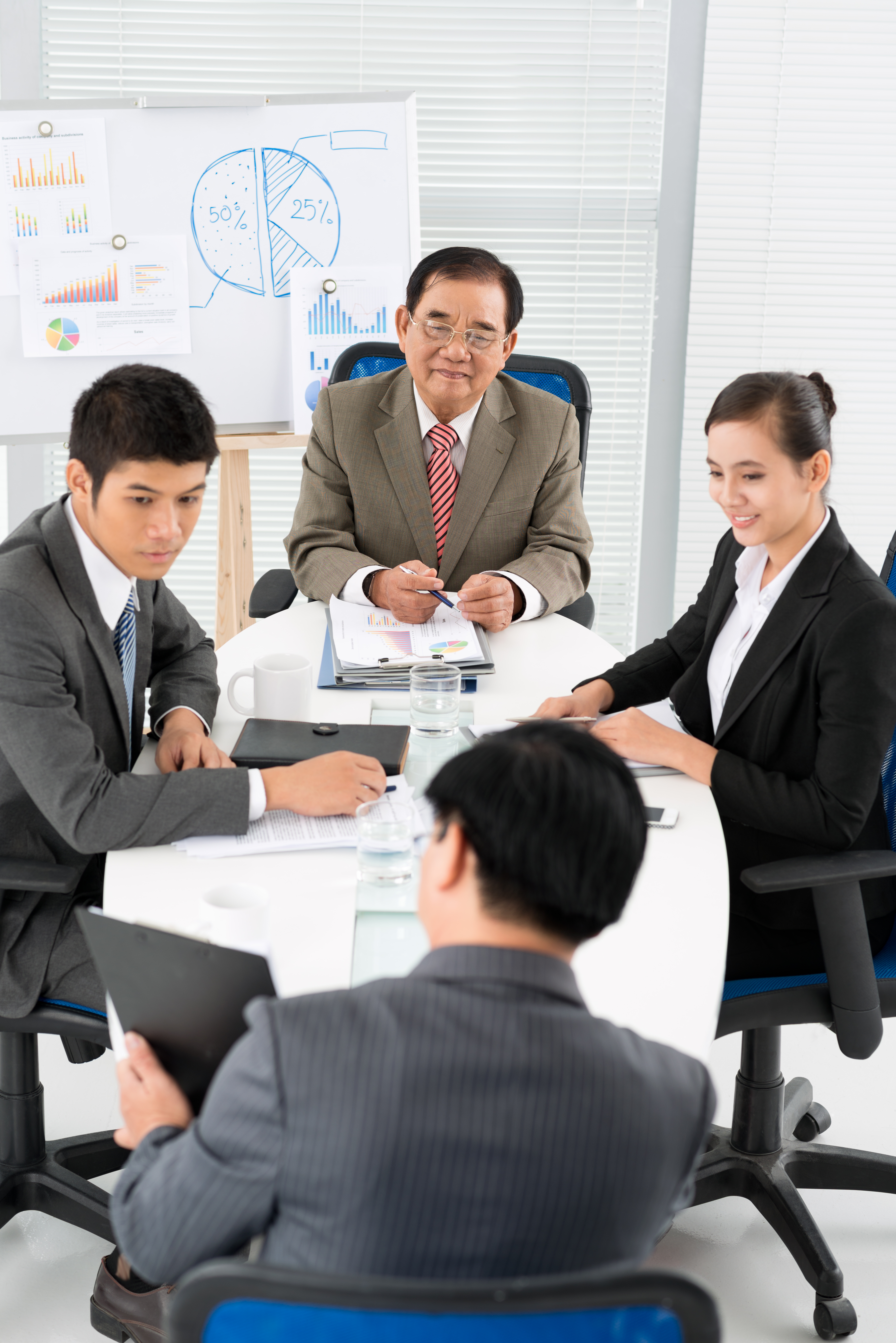 会議室でグラフを背景にチームミーティングを行うビジネスパーソン